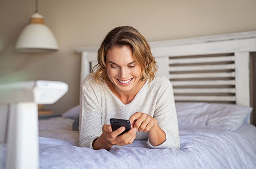 Frau liegt mit Handy auf dem Bett